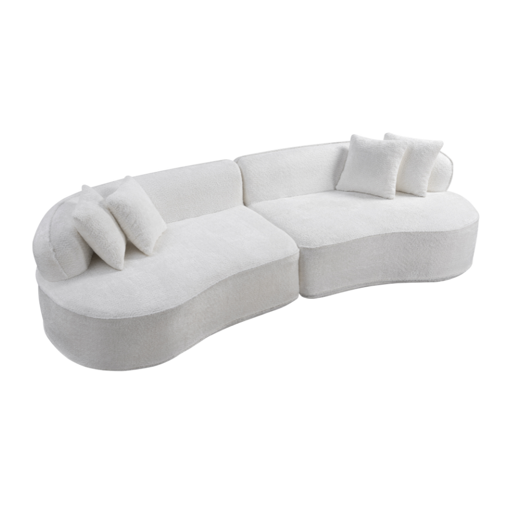 A modern curved modular sofa upholstered in a soft off-white fabric, featuring several matching throw pillows, shown against a plain white background.